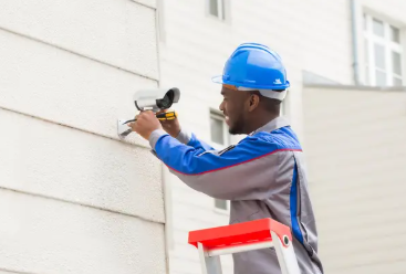 HD security camera mounted on the exterior wall of a building, angled to monitor the entrance; clear sky background, professional CCTV installation, sharp and watchful mood